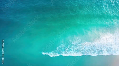 an aerial view of a serene ocean scene with gentle waves rolling towards the shore, the water transitioning from deep blue to light green near the coast