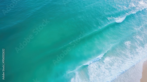 an aerial view of a serene ocean scene with gentle waves rolling towards the shore, the water transitioning from deep blue to light green near the coast