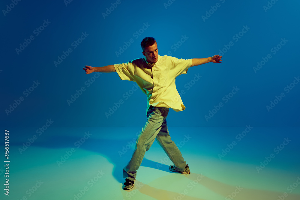 Obraz premium Cool guy, talented and artistic man energetically dancing hip-hop making dynamic performance against gradient blue background in neon light. Concept of street style, contemporary dance, entertainment