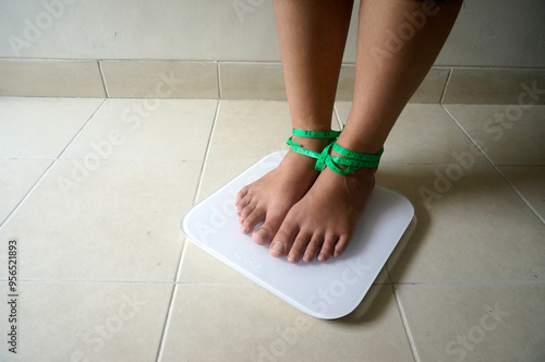 Girl Feet Standing On Digital Weigh Scales Tied Up With Measuring Tape.