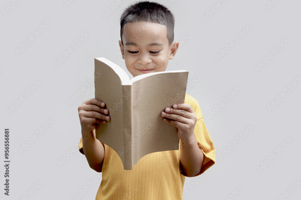 A six year old Asian little boy in a yellow shirt holding book isolated on gray background. Young student kid enjoys reading. Portrait child with school book. Education of kid concept. A six year old Asian little boy in a yellow shirt holding book isolated on gray background. Young student kid enjoys reading. Portrait child with school book. Education of kid concept.