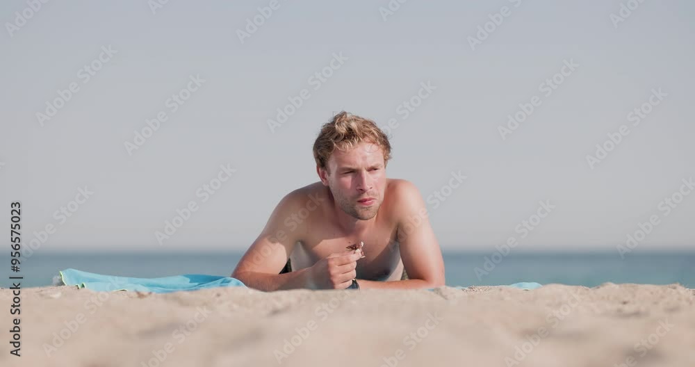 Young man enjoying a donut while relaxing on a sandy beach Young man enjoying a donut while relaxing on a sandy beach