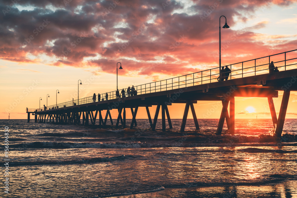 Glenelg Beach jetty with people strolling along at sunset, South Australia Glenelg Beach jetty with people strolling along at sunset, South Australia