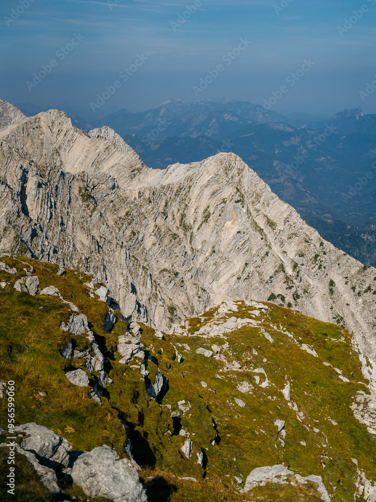 Obraz premium Summit cross on Kleiner Priel with prayer flags, overlooking the rugged peaks of the Gesäuse mountains in Austria. The serene landscape captures the tranquility and majestic beauty of the alpine 