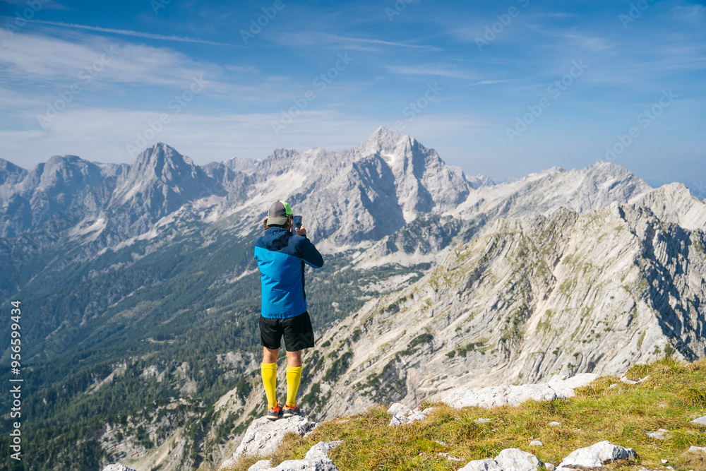Hiker captures the stunning mountain scenery on a smartphone, standing on a rocky outcrop with a backdrop of majestic peaks. Perfect setting for outdoor photography Hiker captures the stunning mountain scenery on a smartphone, standing on a rocky outcrop with a backdrop of majestic peaks. Perfect setting for outdoor photography