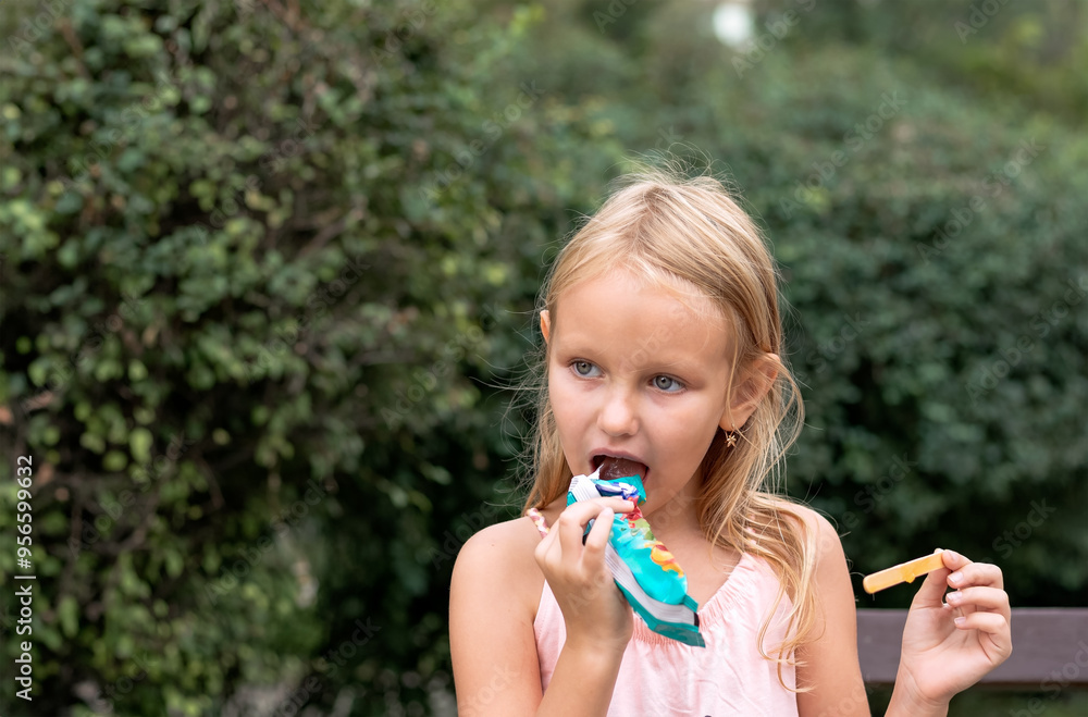 cute blonde girl 6-7 years old sitting on a bench in the park eating ice cream cute blonde girl 6-7 years old sitting on a bench in the park eating ice cream
