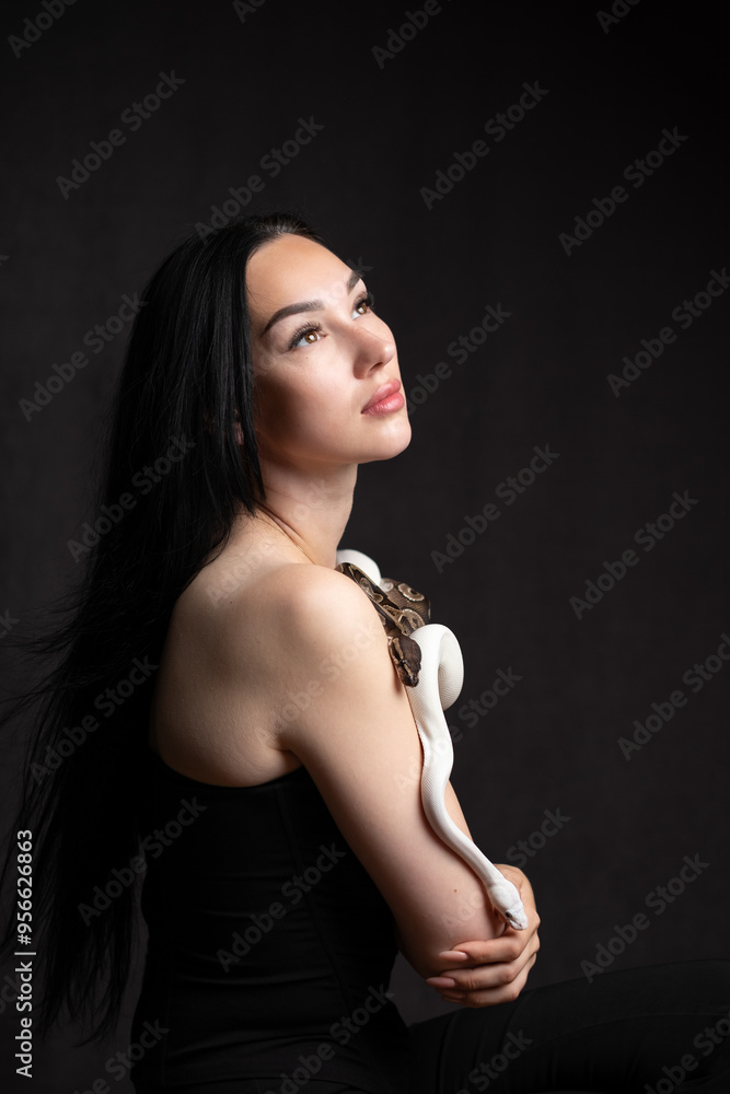 Young beautiful woman with snakes on a plain background. She holds two snakes in her hands. Dark background and copy space Young beautiful woman with snakes on a plain background. She holds two snakes in her hands. Dark background and copy space