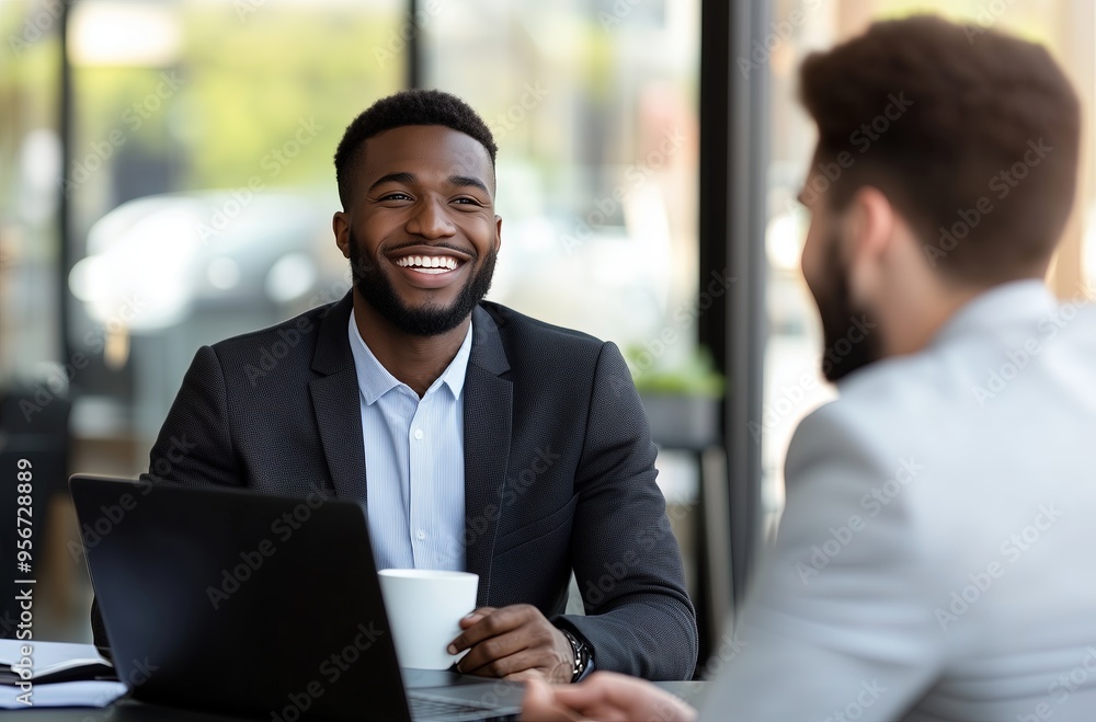 a smiling businessman, talking with a client while working on a laptop during a meeting in the office. a smiling businessman, talking with a client while working on a laptop during a meeting in the office.