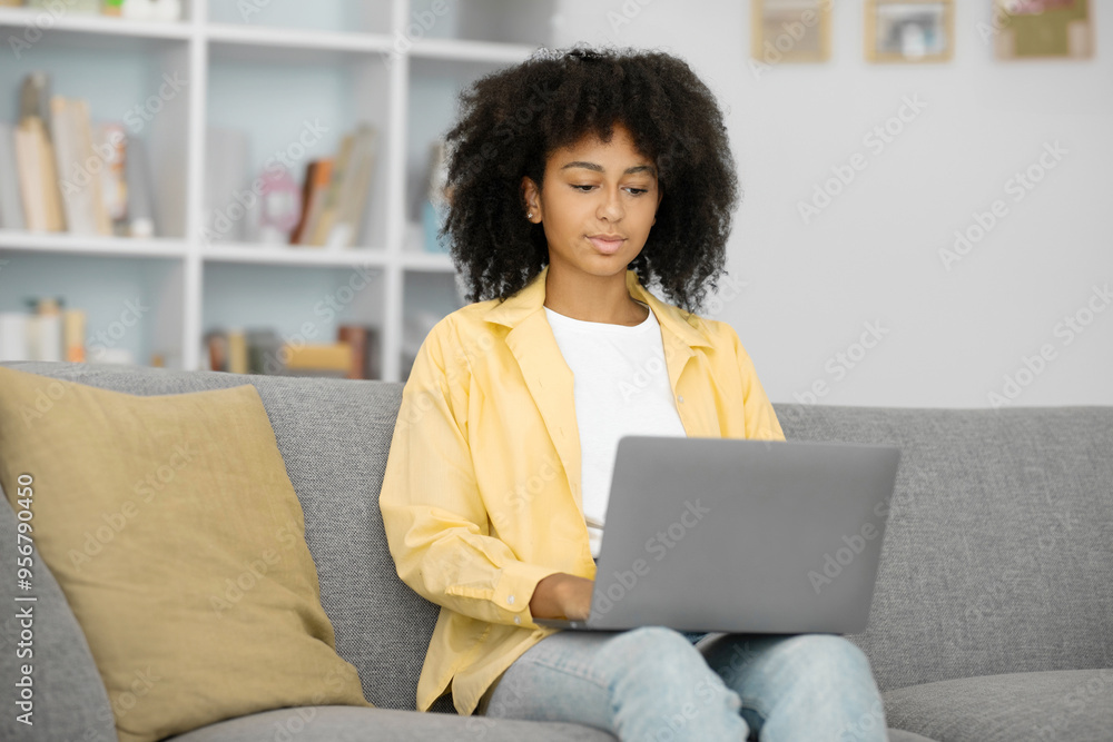 Concentrated curly black lady typing on laptop computer, sitting on sofa in living room interior. Work, freelance and study remotely at home Concentrated curly black lady typing on laptop computer, sitting on sofa in living room interior. Work, freelance and study remotely at home