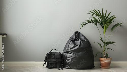 Black bean bag chair, houseplant and backpack near light grey wall in room. Space for text