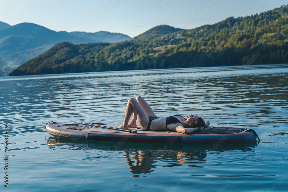 Young cheerful woman relaxing lying on a sup surf board on the water in a mountain lake