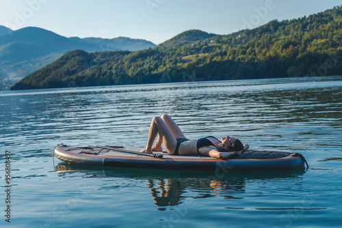 Obraz na płótnie Young cheerful woman relaxing lying on a sup surf board on the water in a mountain lake w salonie