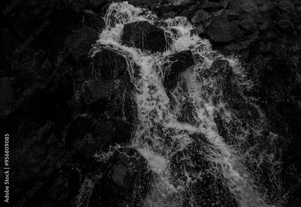 Obraz premium Small stream waterfall running fallen through dark mountain gorge or crevice. black wet Rocks as nature background. Flowing Water of Waterfall in Long Exposure Shot, Natural Backdrop. Sarpi Georgia