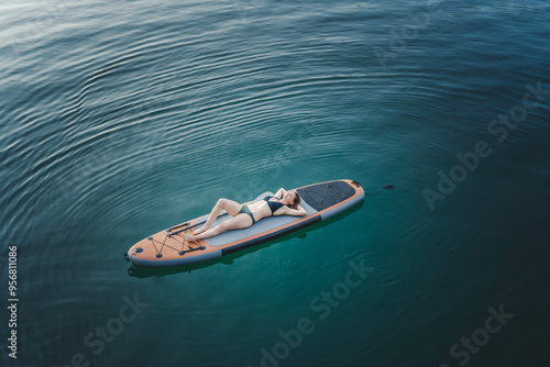 Photography Young cheerful woman relaxing lying down on a sup surf board on the water in a m
