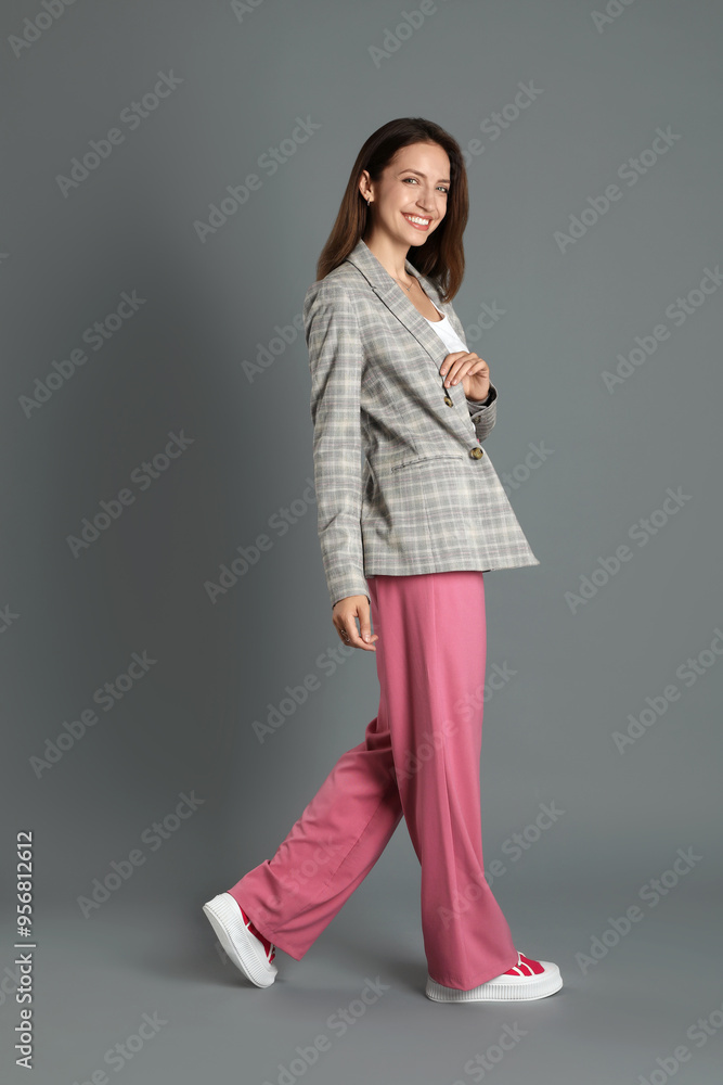 Beautiful woman in stylish jacket and pink pants on grey background Beautiful woman in stylish jacket and pink pants on grey background
