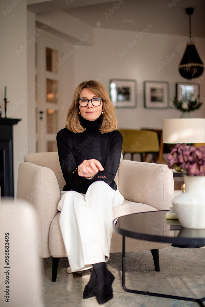 Full length of a mature woman wearing black sweater and pants and sitting in her modern home Full length of a mature woman wearing black sweater and pants and sitting in her modern home