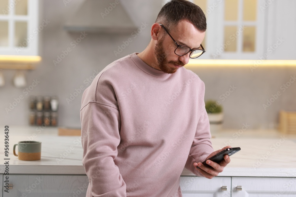 Handsome man looking at smartphone in kitchen Handsome man looking at smartphone in kitchen