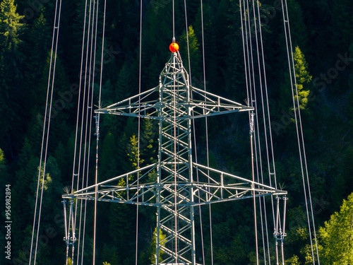 Aerial view of power line pylon in alpine forest in Switzerland. Electric current distribution with power grid.