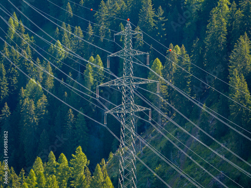 Aerial view of power line pylon in alpine forest in Switzerland. Electric current distribution with power grid.