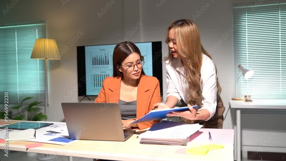 Two asian business women standing and talking about analyzing documents in workplace office