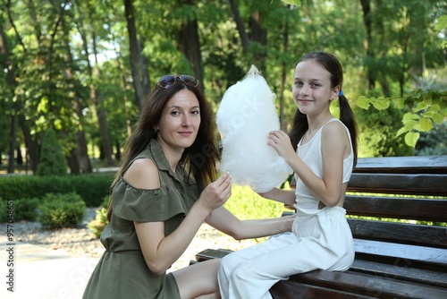 Mother and daughter eating sweet cotton candy on bench in park