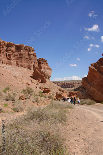 A tourist group walks along the bottom of the Charyn Canyon against the background of the blue sky. South-East of Kazakhstan.