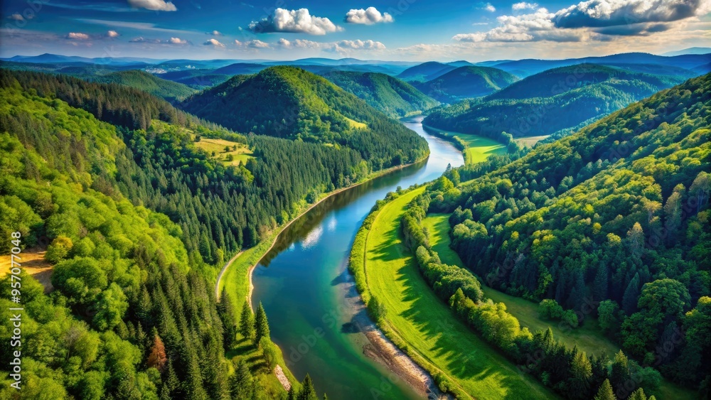 Fototapeta premium Serene aerial view of a winding river flowing through a lush green valley surrounded by dense forests and rugged hills under a clear blue sky.