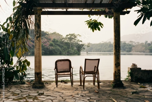 Two wicker chairs peacefully facing a calm lake under a rustic pergola  creating a serene and picturesque scene of tranquility and natural beauty.