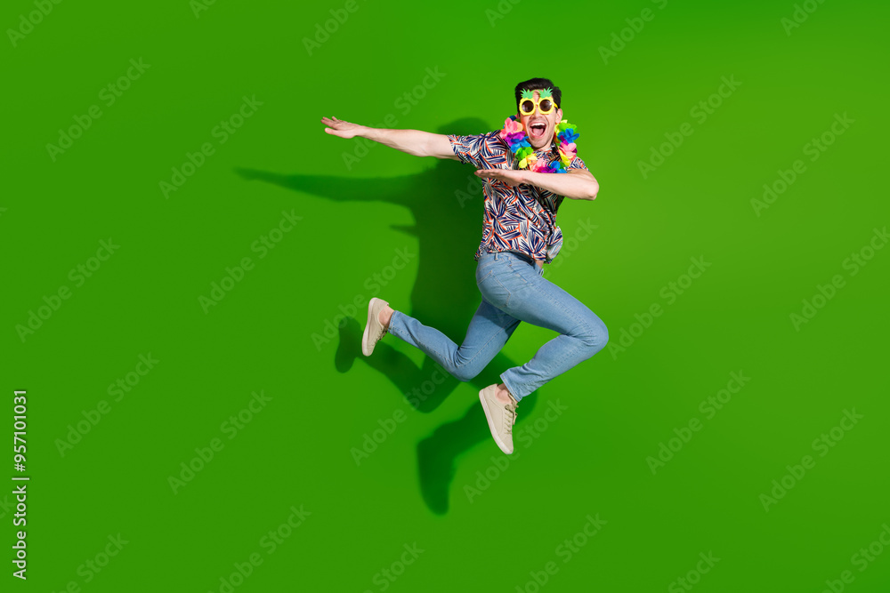 Full size photo of cheerful funky guy dressed print shirt jeans in sunglass necklace jumping dancing isolated on green color background Full size photo of cheerful funky guy dressed print shirt jeans in sunglass necklace jumping dancing isolated on green color background