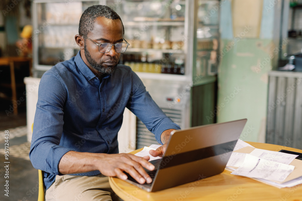 Black self-employed cafe owner typing and watching laptop at table Black self-employed cafe owner typing and watching laptop at table