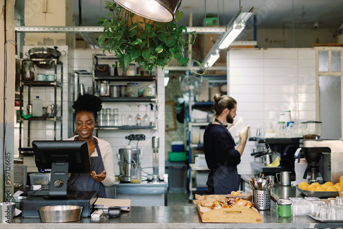 Female cashier or waiter using cash register near waiter in cafe photo