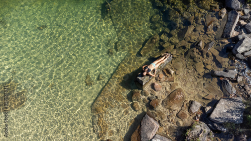 Woman sunbathing on a rock in the middle of crystal-clear waters