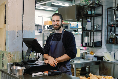 Young positive male ?ashier looking at camera at counter in cafe photo