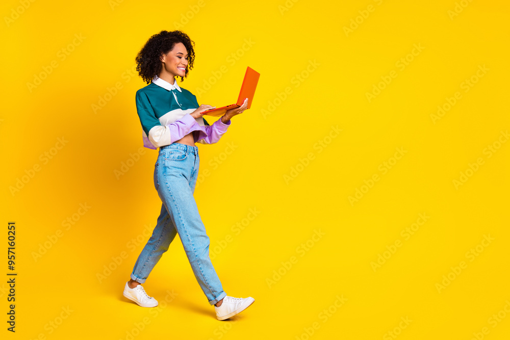 Full size photo of optimistic woman dressed striped top look at laptop walk to empty space isolated on vivid yellow color background Full size photo of optimistic woman dressed striped top look at laptop walk to empty space isolated on vivid yellow color background