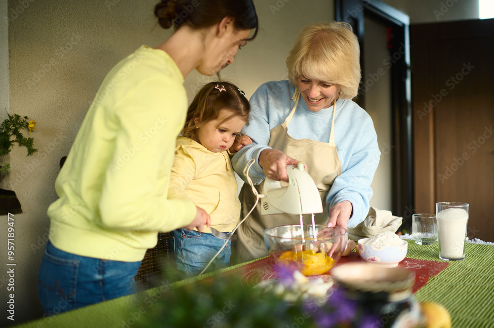 Cheerful kid girl helping granny and mom to bake in home kitchen Cheerful kid girl helping granny and mom to bake in home kitchen
