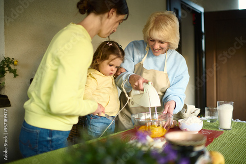 Cheerful kid girl helping granny and mom to bake in home kitchen photo