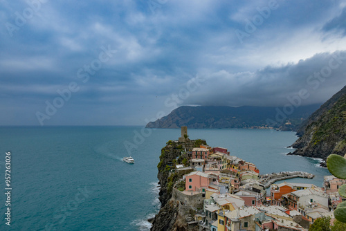 Horizontal shot capturing a boat approaching the shore from afar, with vibrant, colorful buildings lining the waterfront in an idyllic Italian town. The scene exudes a sense of stillness and serenity