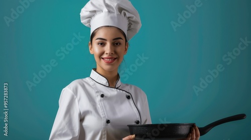 Professional Female Chef in Uniform Holding a Frying Pan Against a Teal Background photo