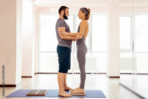 Man helping woman to stand on sadhu yoga board