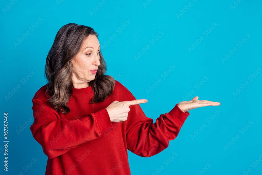 Photo of pretty aged lady indicate finger hold empty space wear red pullover isolated on blue color background Photo of pretty aged lady indicate finger hold empty space wear red pullover isolated on blue color background