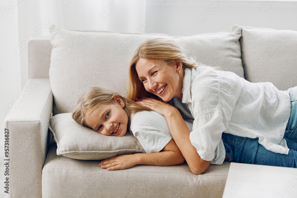 Mother and daughter relaxing together on a comfortable white couch in a cozy living room setting Mother and daughter relaxing together on a comfortable white couch in a cozy living room setting