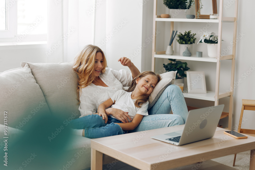 Mother and daughter bonding on couch with laptop and book in cozy living room Mother and daughter bonding on couch with laptop and book in cozy living room
