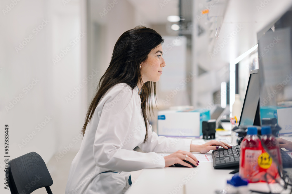 Pharmacist focused on work at computer in modern pharmacy workplace Pharmacist focused on work at computer in modern pharmacy workplace