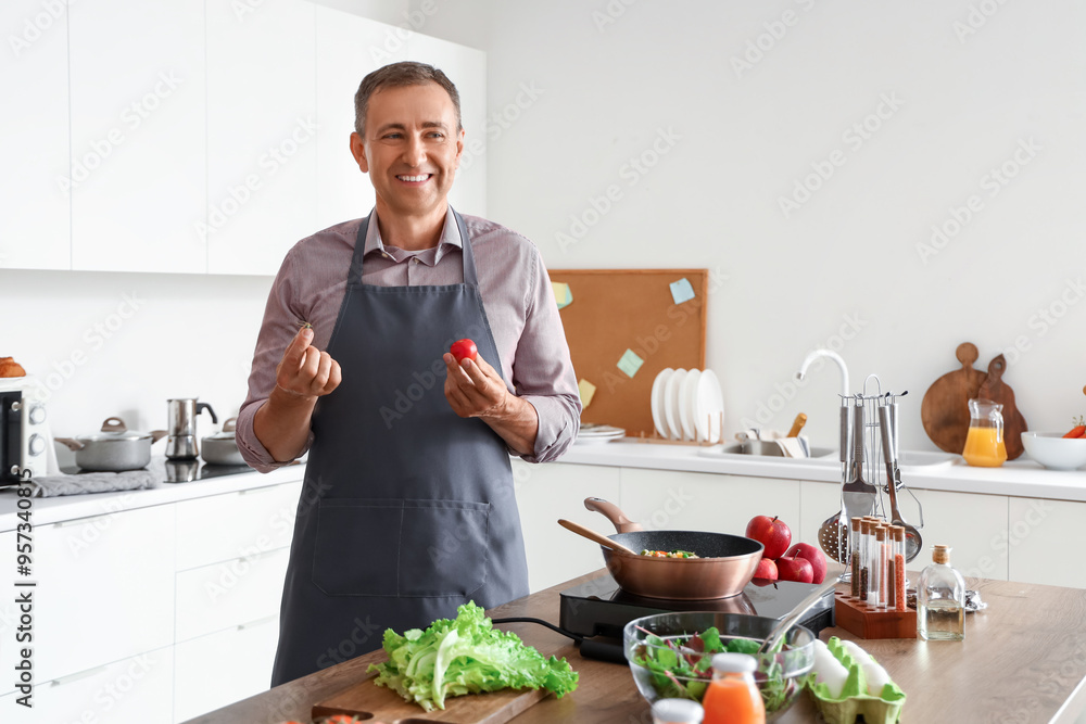 Mature man with fresh tomato in kitchen Mature man with fresh tomato in kitchen