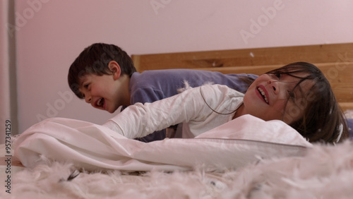 Siblings Laughing And Playing On A Bed Covered In Feathers, Enjoying The Fun And Excitement Of A Pillow Fight In A Warm And Cozy Bedroom Setting photo