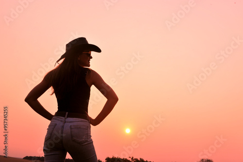 silhueta de linda vaqueira usando chapéu em pôr do sol  photo