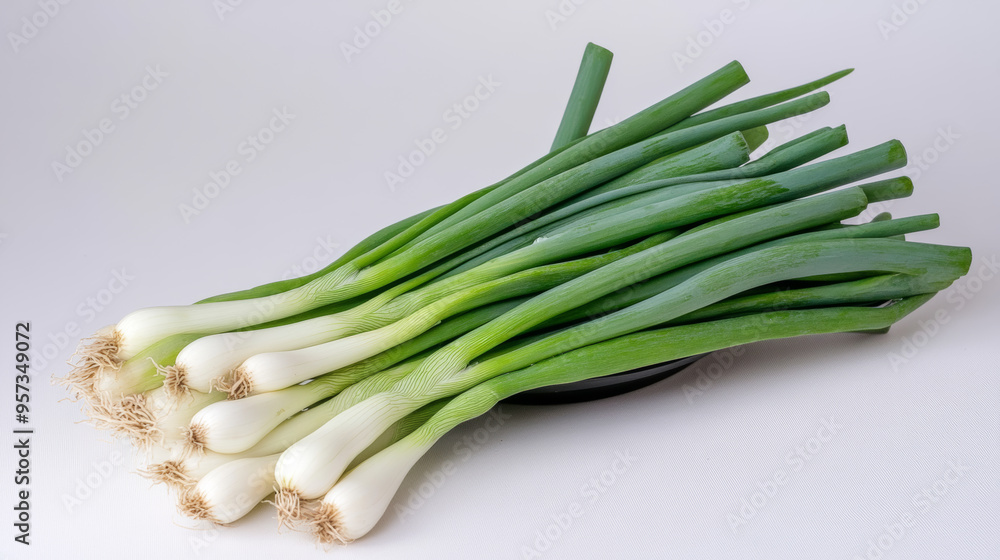 A bunch of green onions sits in a black bowl against a white backdrop. A bunch of green onions sits in a black bowl against a white backdrop.