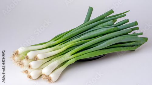 A bunch of green onions sits in a black bowl against a white backdrop.