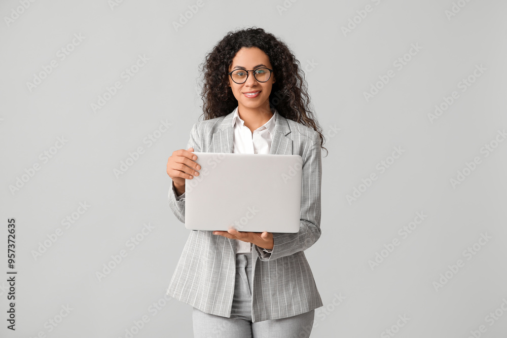 Young African-American businesswoman with modern laptop on grey background Young African-American businesswoman with modern laptop on grey background