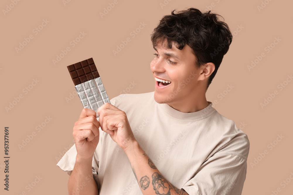 Handsome young man with sweet chocolate bar on brown background Handsome young man with sweet chocolate bar on brown background